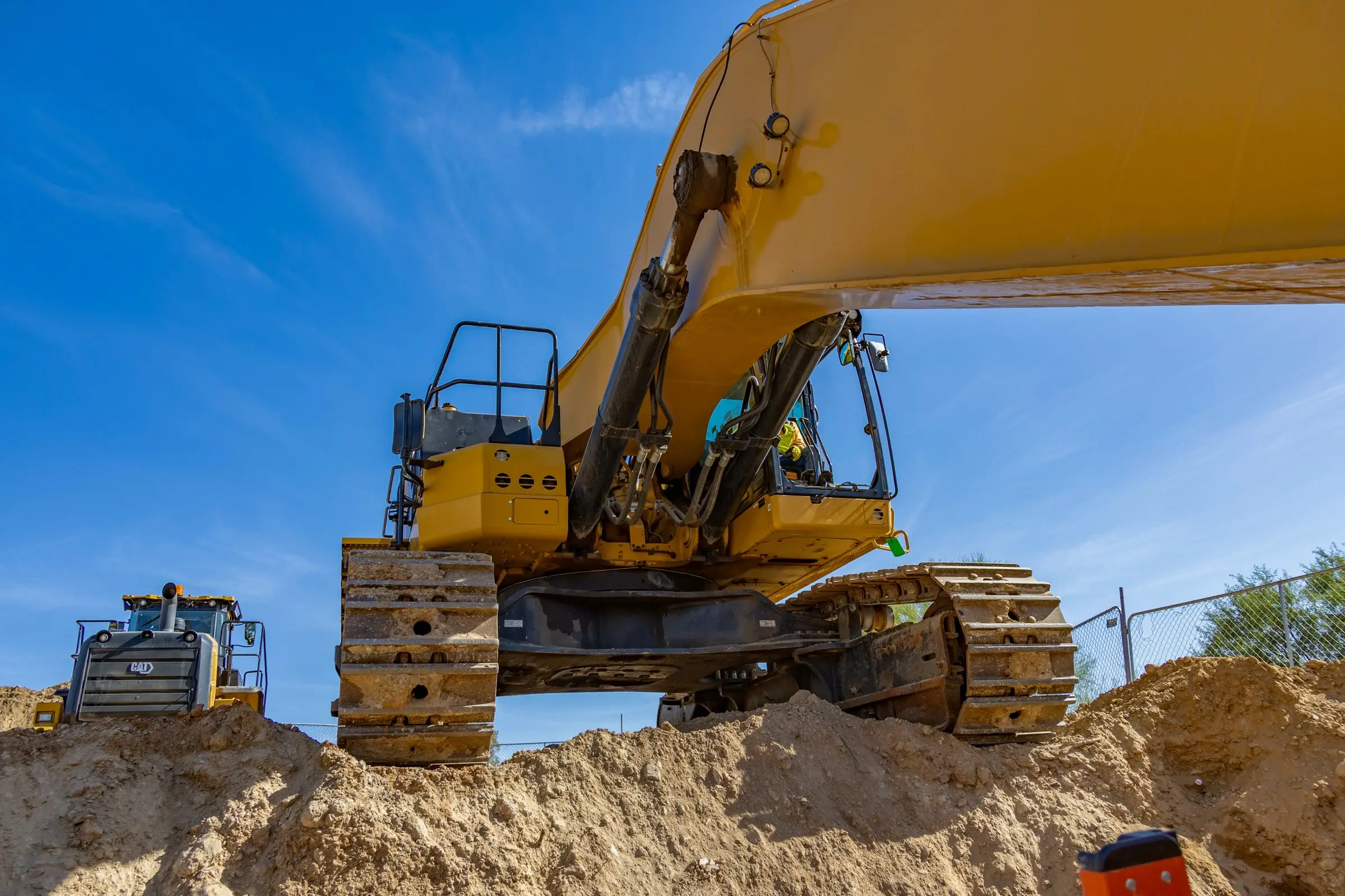 Yellow excavator digging at a Phoenix construction site under a blue sky