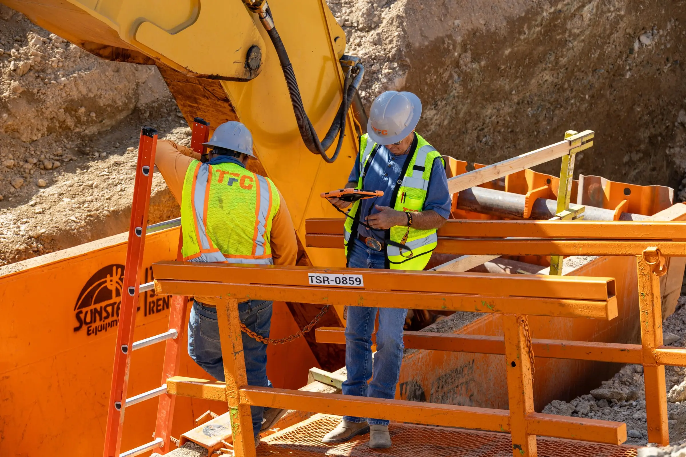 Two construction workers reviewing plans inside a trench box