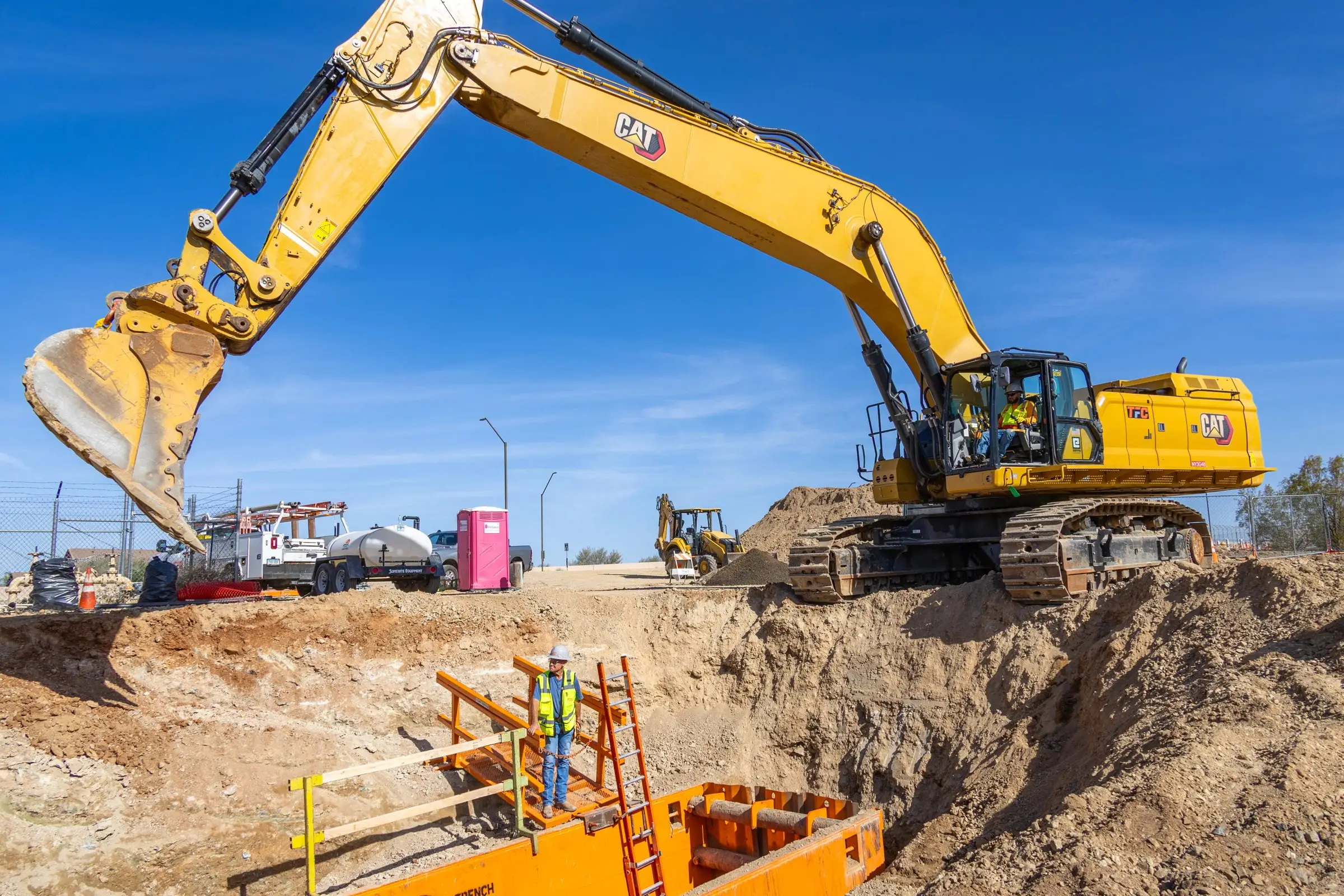 Excavator and trench box with a worker on the ladder